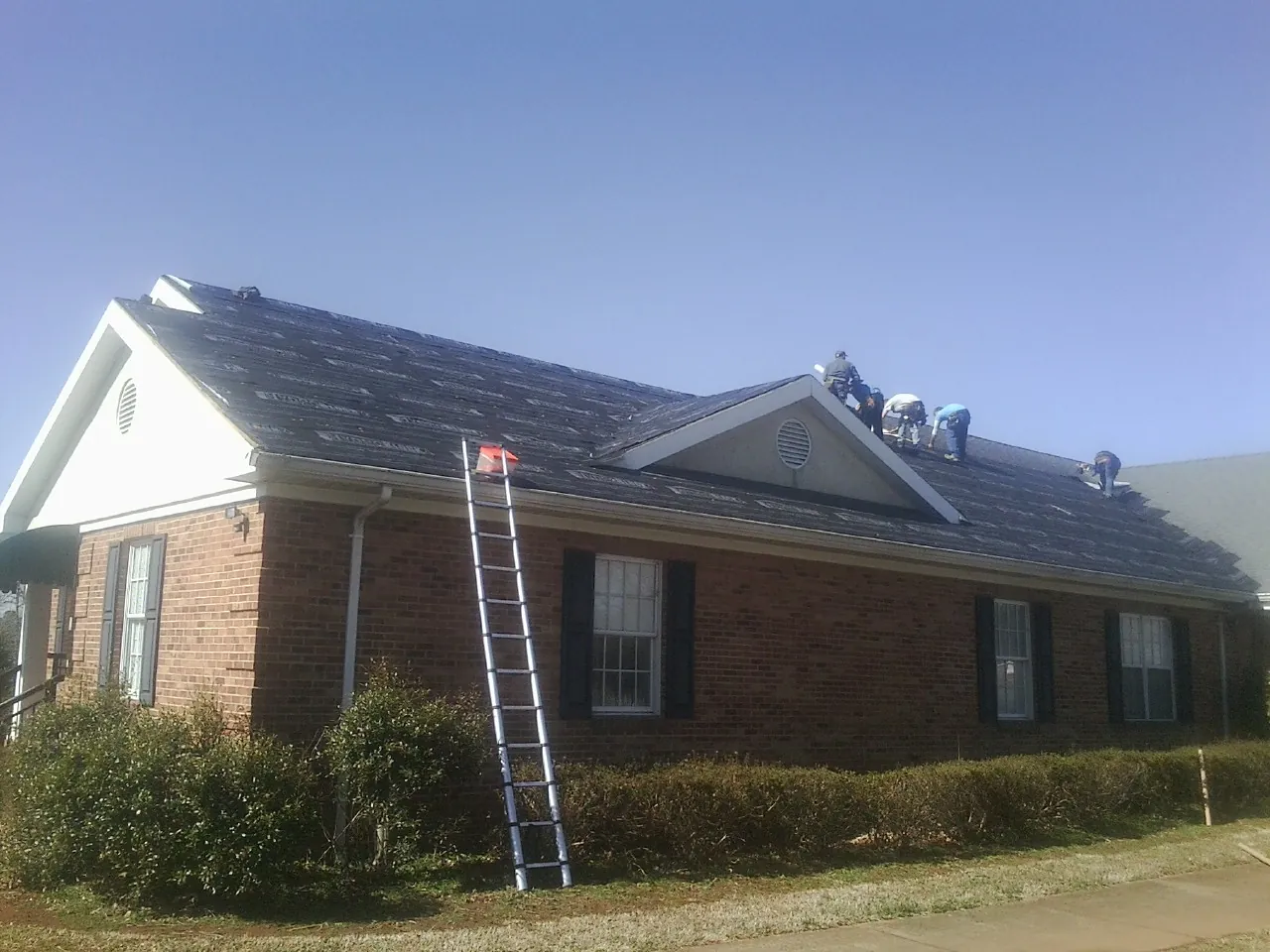Crew tearing shingles off a brick ranch roof with a ladder set — Emergency Roof Repair work by our crew in Pocono Pines