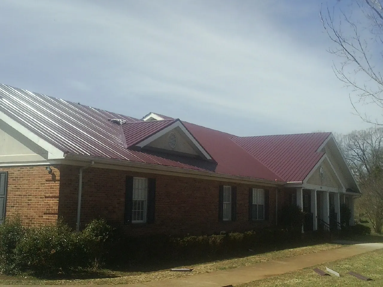 Red metal roof with gabled entries on a long brick building, from a Hail Damage Roof Repair job in Pocono Pines