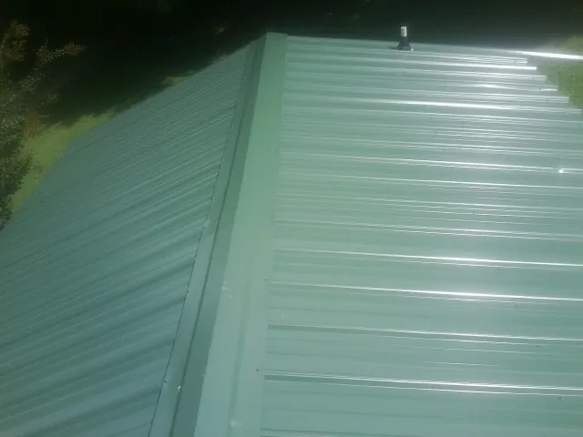 New green metal panels meeting at the ridge of a roof — Flat Roof Repair work by our crew in Pocono Pines