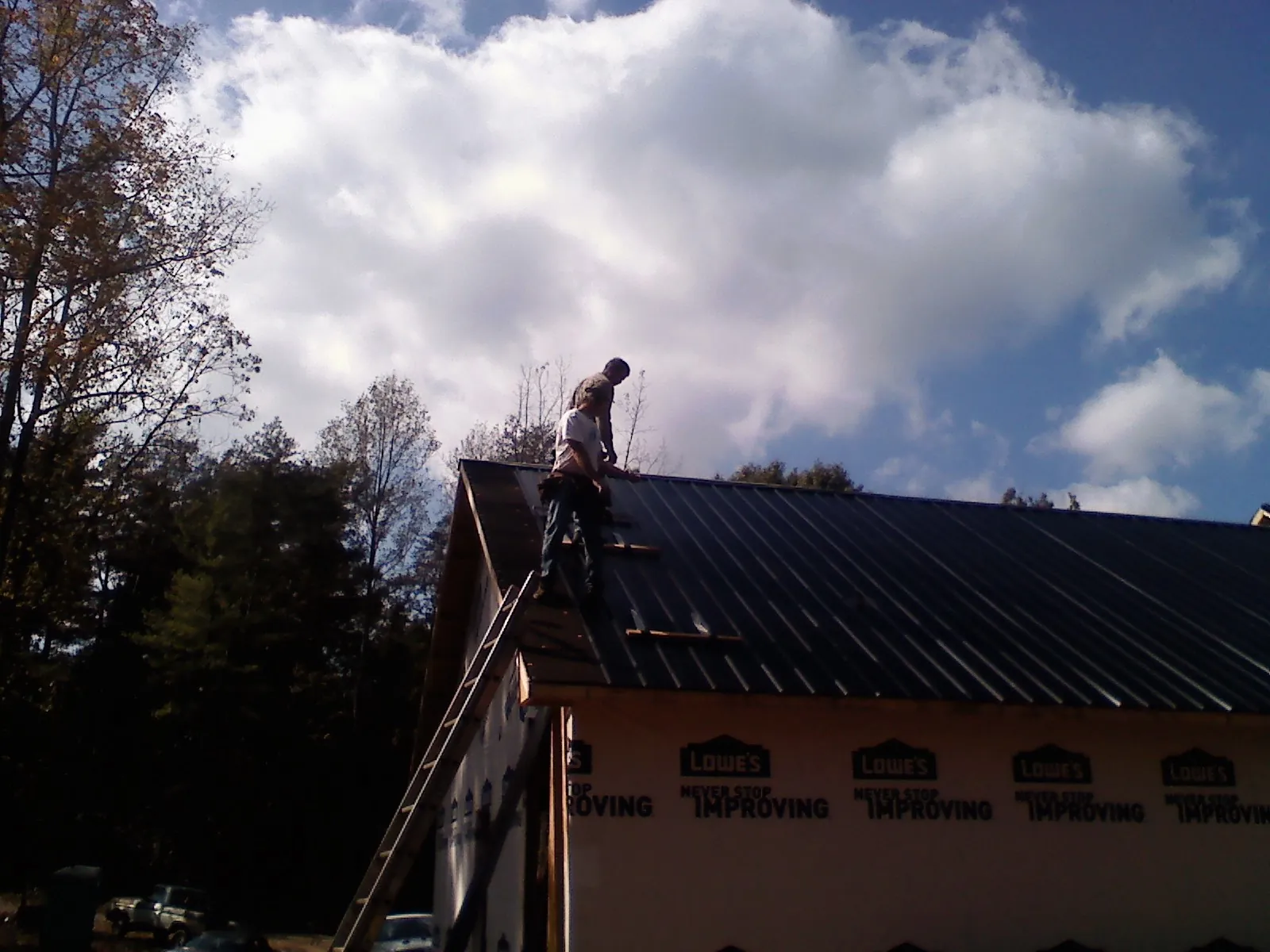 Roofer fastening dark metal panels high against a cloudy sky, from a Roof Inspection job in Pocono Pines