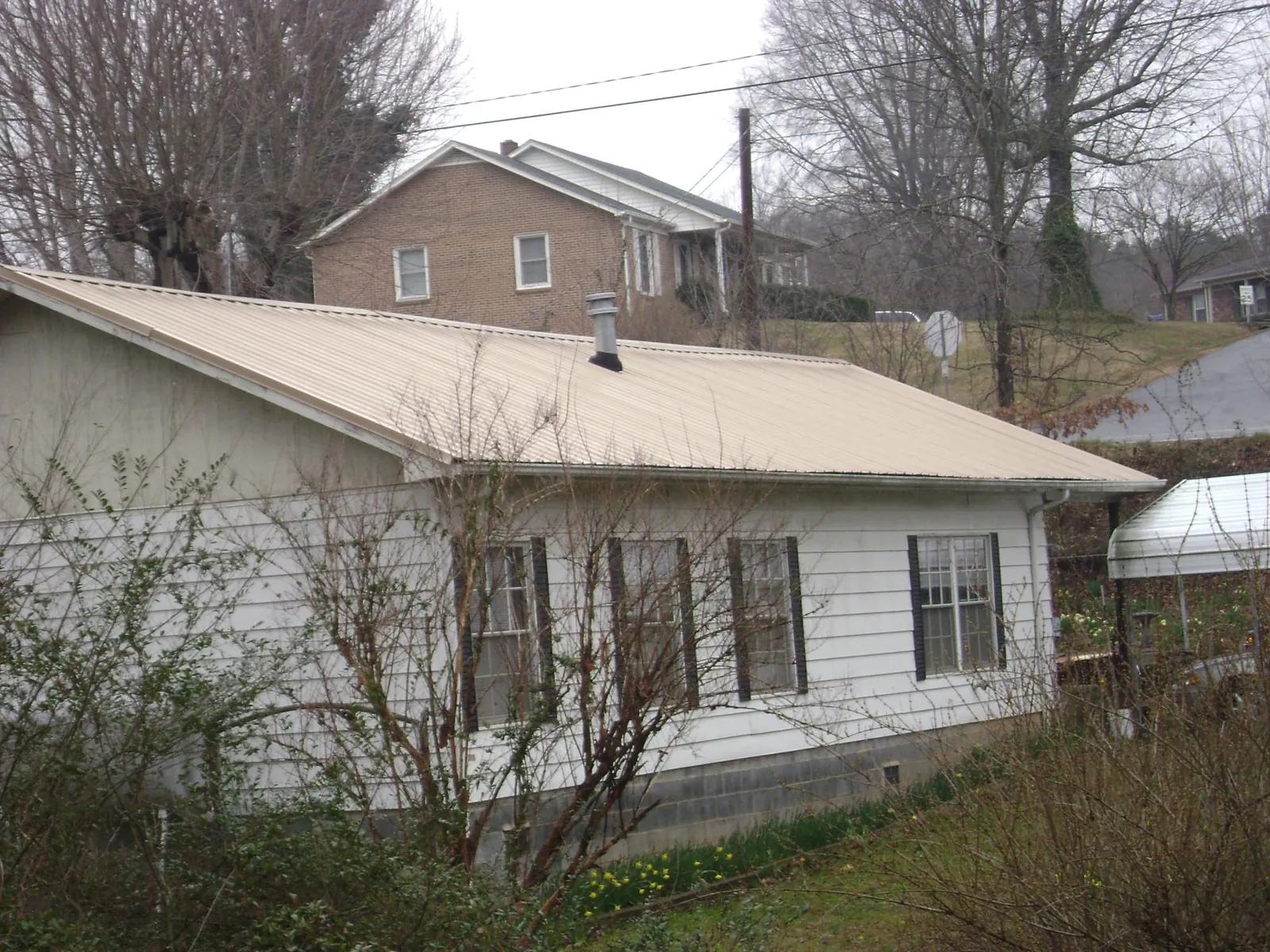Tan metal roof on a white sided house set into a hillside — Commercial Roofing by Roofing Brothers in Pocono Pines