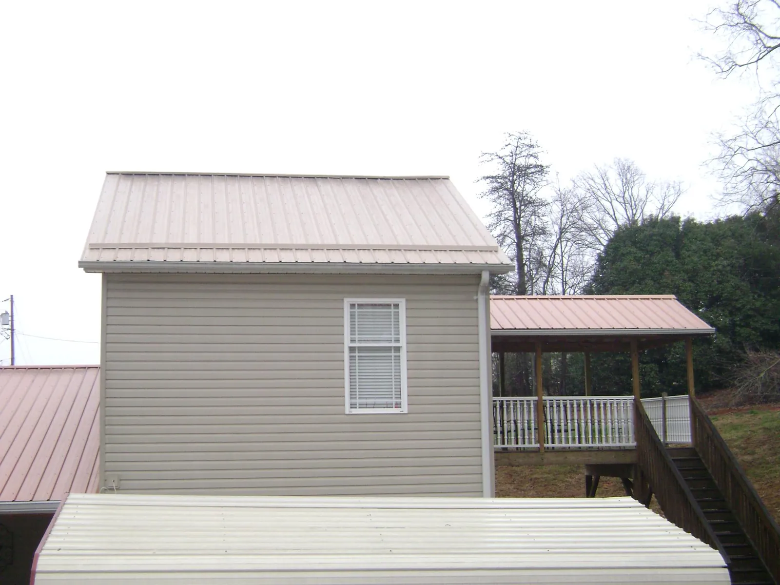 Tan metal roofs on a two story addition and attached porch, from a Roof Replacement job in Pocono Pines